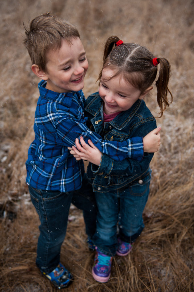 A young boy hugs his sister playfully in the grass.