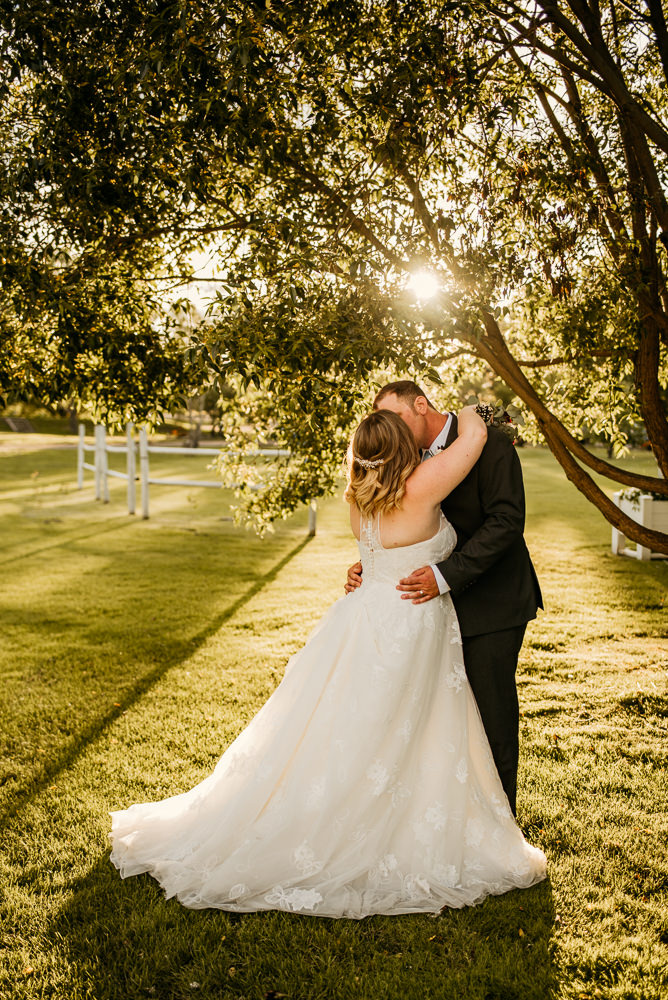 bride and groom kissing under a tree at sunset