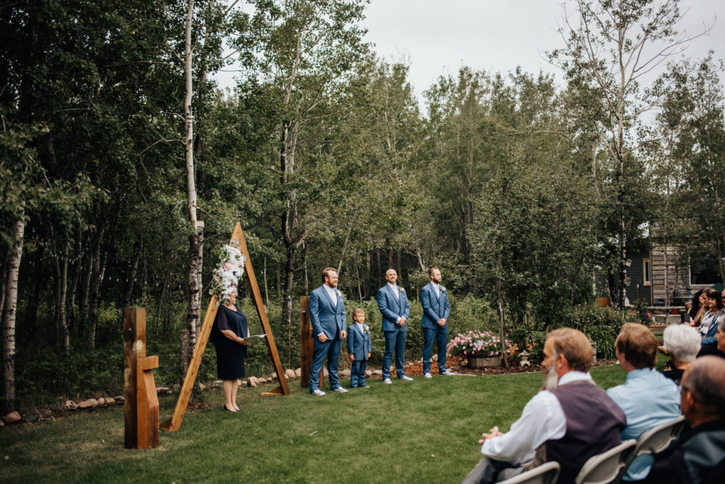 groom and groomsmen in blue suits at altar before backyard wedding ceremony