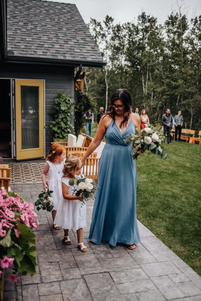 bridesmaid in blue dress and flower girls entering backyard wedding ceremony