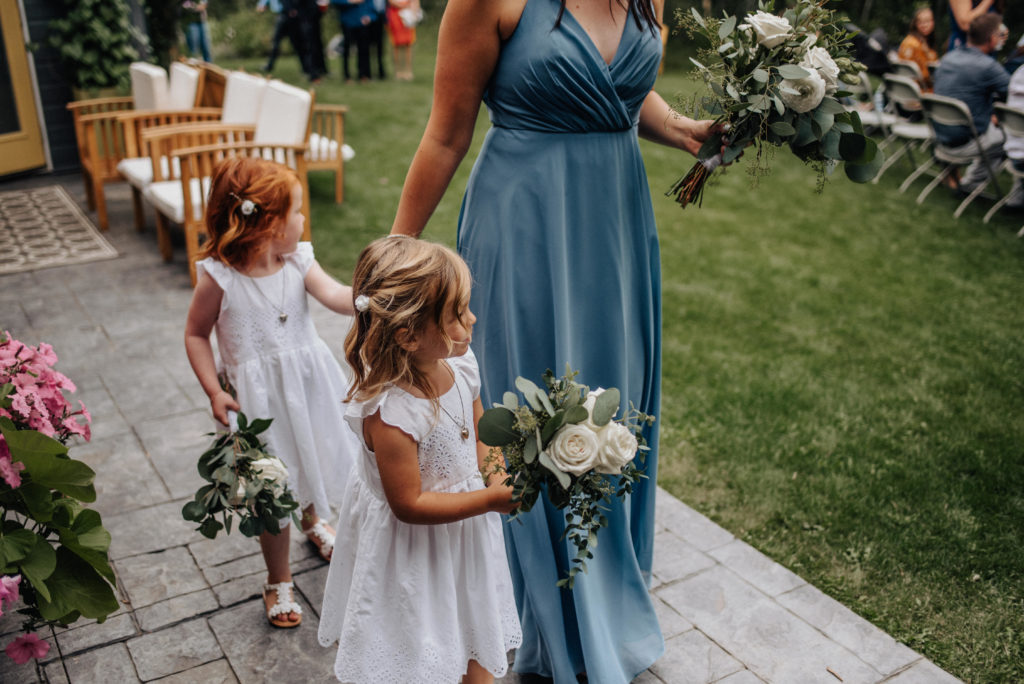 bridesmaid in blue dress and flower girls entering backyard wedding ceremony